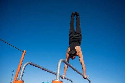 Shirtless man doing handstand on parallel bars at sports ground. Stock Photos