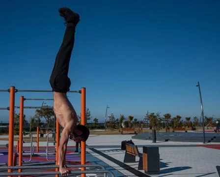 Shirtless man doing handstand on parallel bars at sports ground. Stock Photos