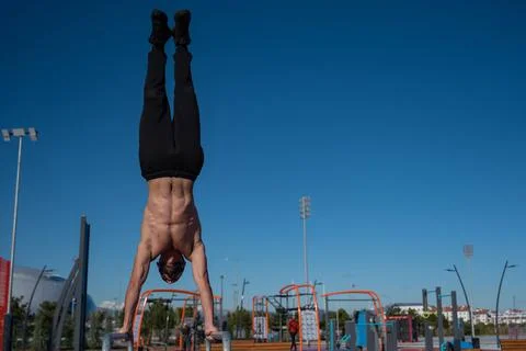 Shirtless man doing handstand on parallel bars at sports ground. Stock Photos