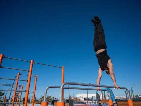 Shirtless man doing handstand on parallel bars at sports ground. Stock Photos