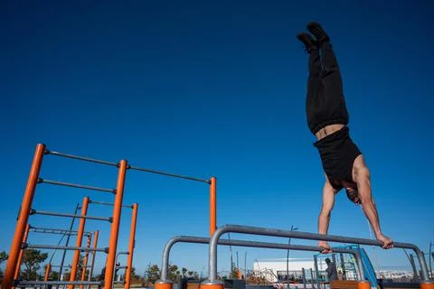 Shirtless man doing handstand on parallel bars at sports ground. Stock-Fotos