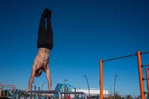 Shirtless man doing handstand on parallel bars at sports ground. Stock Photos