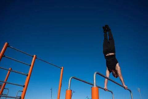 Shirtless man doing handstand on parallel bars at sports ground. Foto stock