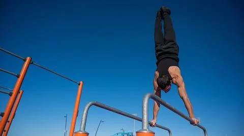 Shirtless man doing handstand on parallel bars at sports ground. Stock Photos