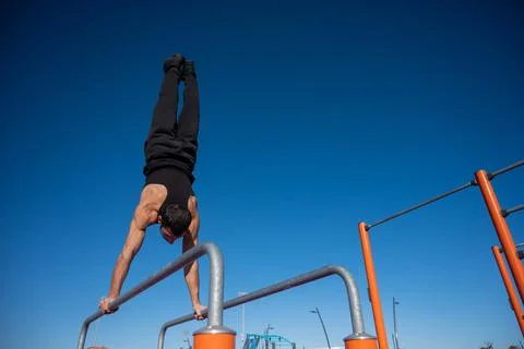Shirtless man doing handstand on parallel bars at sports ground. Stock-Fotos