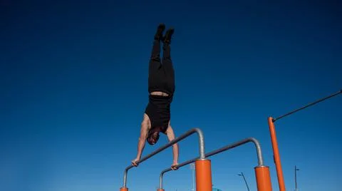 Shirtless man doing handstand on parallel bars at sports ground. Stock Photos