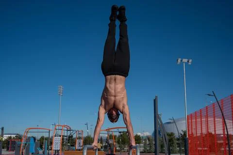 Shirtless man doing handstand on parallel bars at sports ground. 写真素材