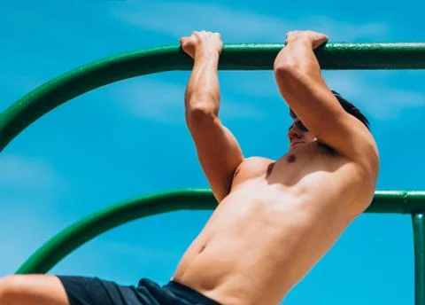 Shirtless man doing pull-ups on horizontal bar 库存照片