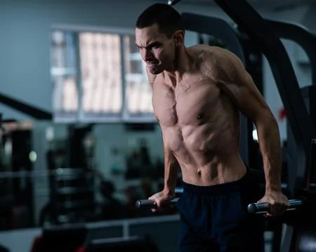 Shirtless man doing triceps dips from parallel bars in gym. Stock Photos