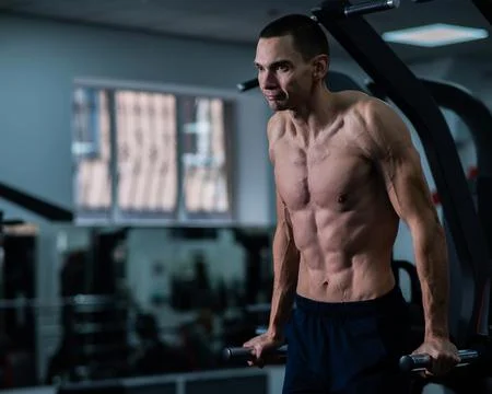 Shirtless man doing triceps dips from parallel bars in gym. Stock Photos
