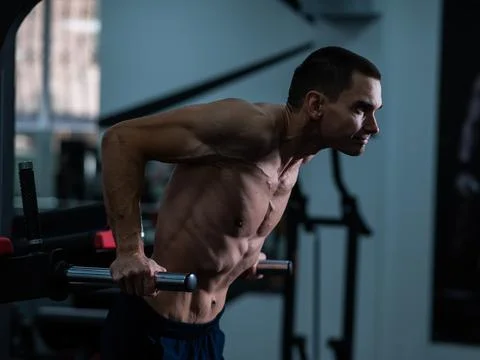 Shirtless man doing triceps dips from parallel bars in gym. Stock Photos