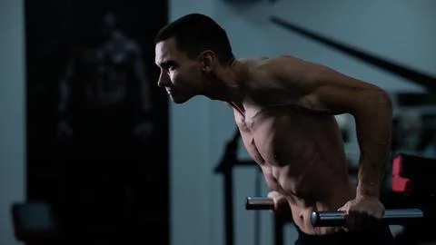 Shirtless man doing triceps dips from parallel bars in gym. Stock Photos