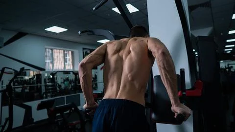 Shirtless man doing triceps dips from parallel bars in gym. Stock Photos