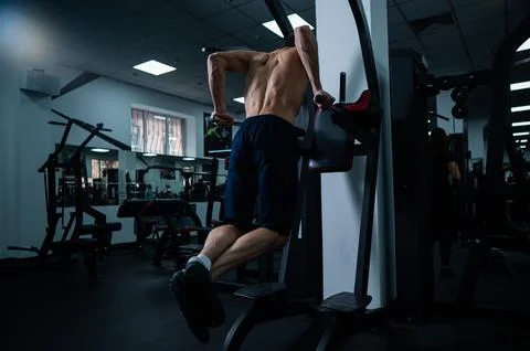 Shirtless man doing triceps dips from parallel bars in gym. Stock Photos