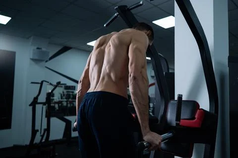 Shirtless man doing triceps dips from parallel bars in gym. Stock Photos