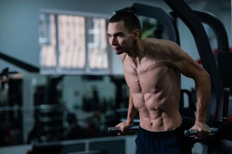 Shirtless man doing triceps dips from parallel bars in gym. Stock Photos