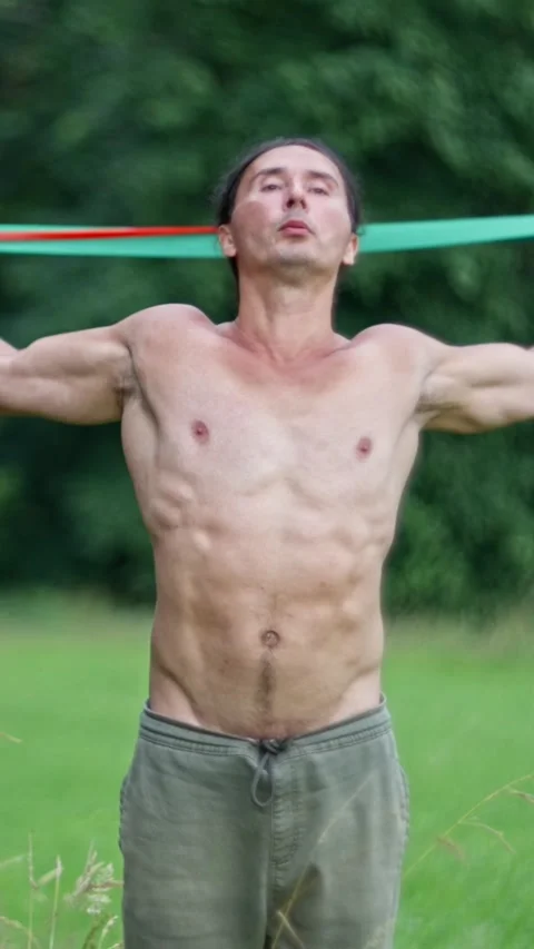 A shirtless man is energetically performing resistance band exercises outdoors Stock Footage 308928212