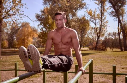 Shirtless man exercising on parallel bars at park Stock Photos