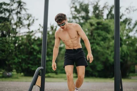 Shirtless man exercising on parallel bars in outdoor park for fitness and Stock-Fotos