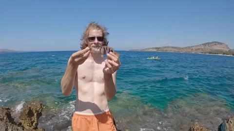 Shirtless man holding caught fish while sea shore fishing in Adriatic sea Stock Footage 276229136