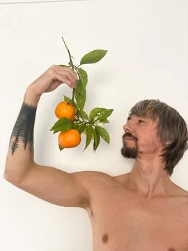 Shirtless man holding an orange branch with fresh fruit Foto stock