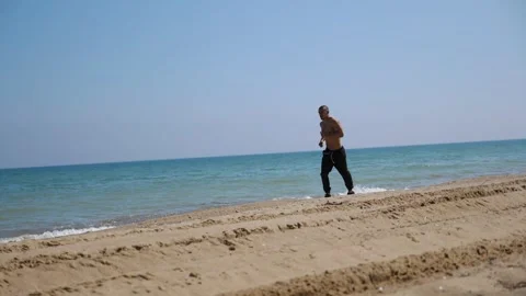 Shirtless man jogging along sandy beach, showcasing dynamic movement and energy Vidéo 332851606