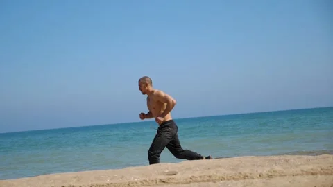 Shirtless man jogging along sandy beach, showcasing dynamic movement and energy Vidéo 332851810