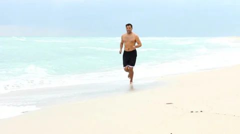 Shirtless man running on beach Stock Footage 33577763