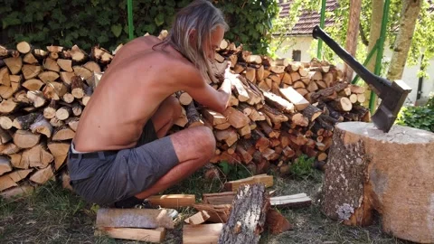 Shirtless man stacking firewood log pile chopped with axe in backyard Stock Footage 345124037