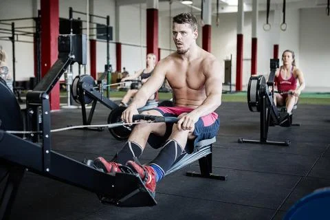 Shirtless Man Using Rowing Machine In Gymnasium Stockfoto's