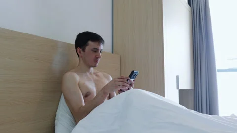 Shirtless man using a smartphone in bed 库存影片 335369758