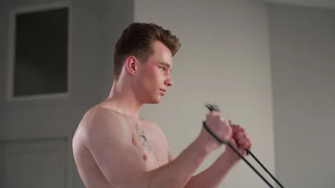 Shirtless student pulls resistance rope in minimalist room workout muscle focus Stock Footage 308660386