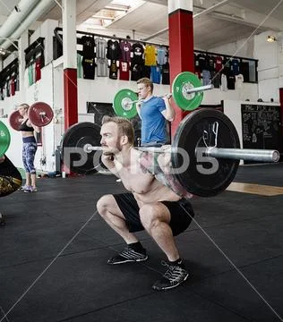 Shirtless Trainer Lifting Barbell While Crouching In Gym Stock Photos