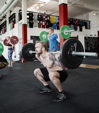 Shirtless Trainer Lifting Barbell While Crouching In Gym Stock Photos