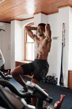 Shirtless young black man doing intense cardio workout on exercise bike at the Stock Photos