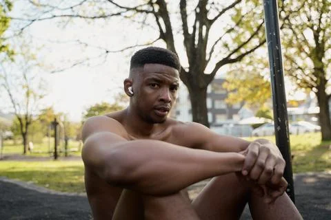 Shirtless young black man with wireless earphones sitting and looking at camera Stock Photos