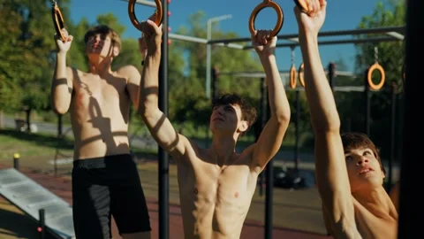 Shirtless Young guys doing pull ups on gymnastic rings at the sports park. Stock Footage 346141385