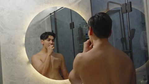 Shirtless Young Man Brushing Teeth in Modern Bathroom Mirror Видео 345100107