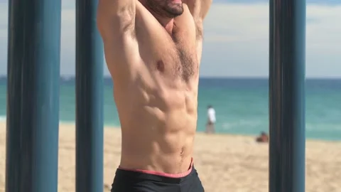 Shirtless young man doing sit-ups on a bar in a park at the beach. Stock Footage 229727787