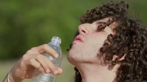 Shirtless young man drinks water after a long walk in the  sun Stock Footage 240397344