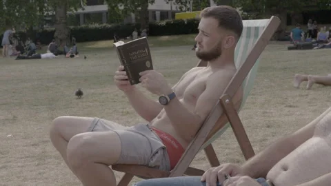 Shirtless Young Man Reading Book in Park Deckchair Stock Footage 344616872