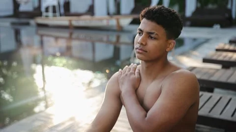 Shirtless young man touching his shoulder in contemplation or pain near pool Stock Footage 328160026