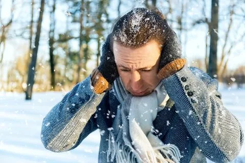 Shivering man stands outdoor in freezing winter weather. He covers his ears.. Stock Photos