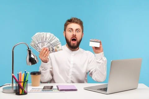 Shocked bearded man office worker holding dollar cash and credit card looking Stock Photos