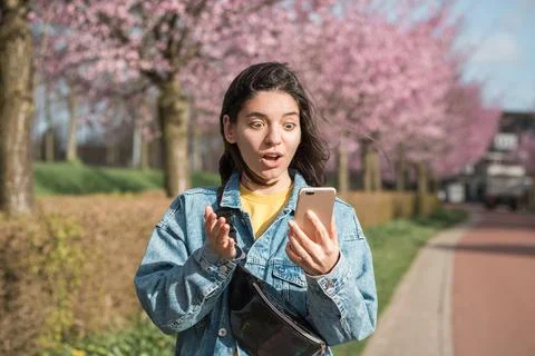 Shocked face expression of a mixed races woman looking into the phone while Stock Photos