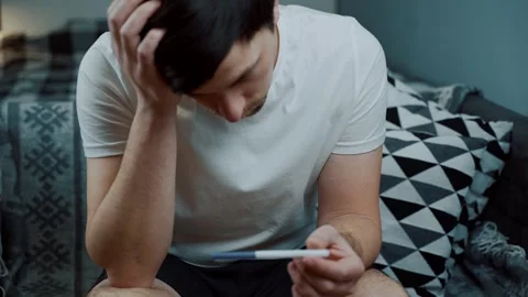 Shocked man looking at a pregnancy test with terror in his eyes. Depicting the Stock Footage 329276560