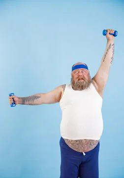 Shocked obese man does exercises with dumbbells training hard in studio Foto stock