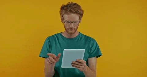 Shocked redhead man in glasses using digital tablet isolated on yellow Stock Footage 136182677
