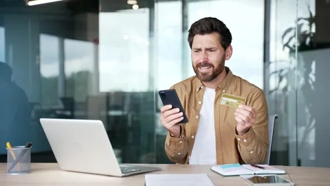 Shocked upset businessman checks his credit card on laptop while sitting at work Stock Footage 295042453