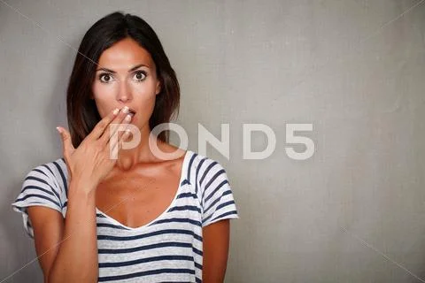 Shocked woman in casual clothing looking at camera with hand to mouth - copy Stock Photos